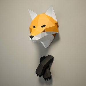 May include: A geometric paper fox head wall decoration in orange, white, and black. The fox head is mounted on a wall, with the fox's paws below. The fox head is orange with white accents and black eyes and nose. The paws are black.