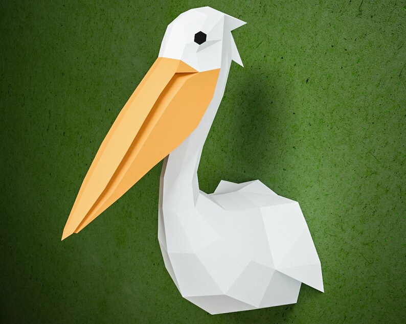 May include: A white paper origami pelican with an orange beak. The pelican is facing to the right and has a green background.
