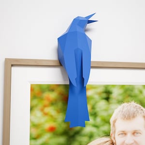 May include: A blue paper bird sculpture perched on a wooden picture frame. The frame contains a photo of a couple.