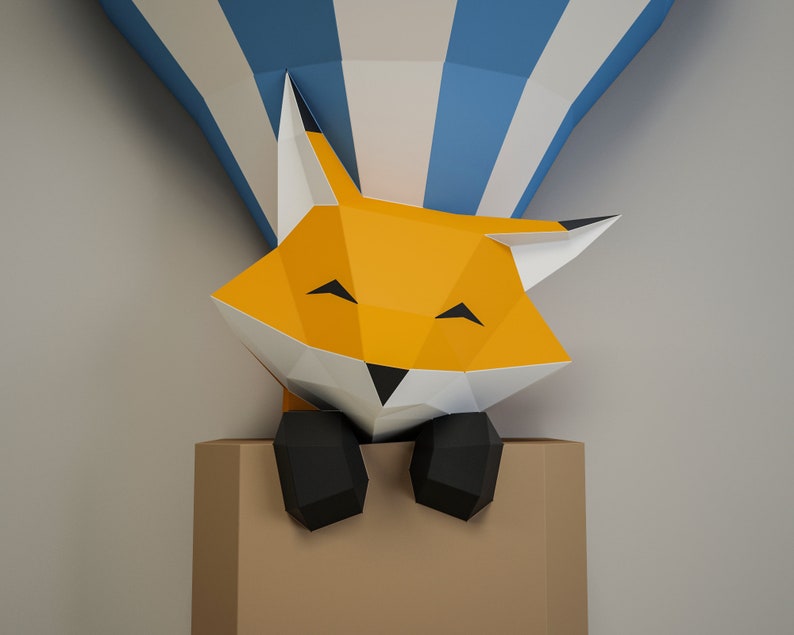 May include: A papercraft fox with orange fur, black eyes, and a black nose peeks out of a brown box. The fox is smiling and has its paws resting on the edge of the box. The fox is partially obscured by a blue and white striped hot air balloon.