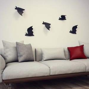 May include: A white couch with three gray pillows and one red pillow. The wall behind the couch is white and has five black bat silhouettes.