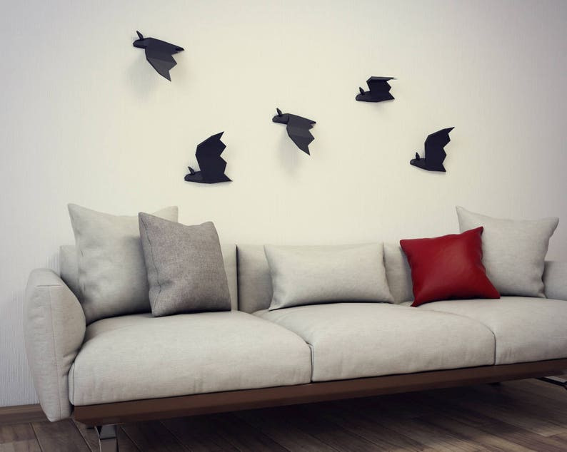 May include: A white couch with three gray pillows and one red pillow. The wall behind the couch is white and has five black bat silhouettes.