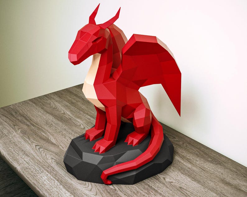 May include: A red geometric dragon sculpture on a black base. The dragon features large wings, horns, and a long tail. The sculpture is made of paper or card and sits on a wooden surface.