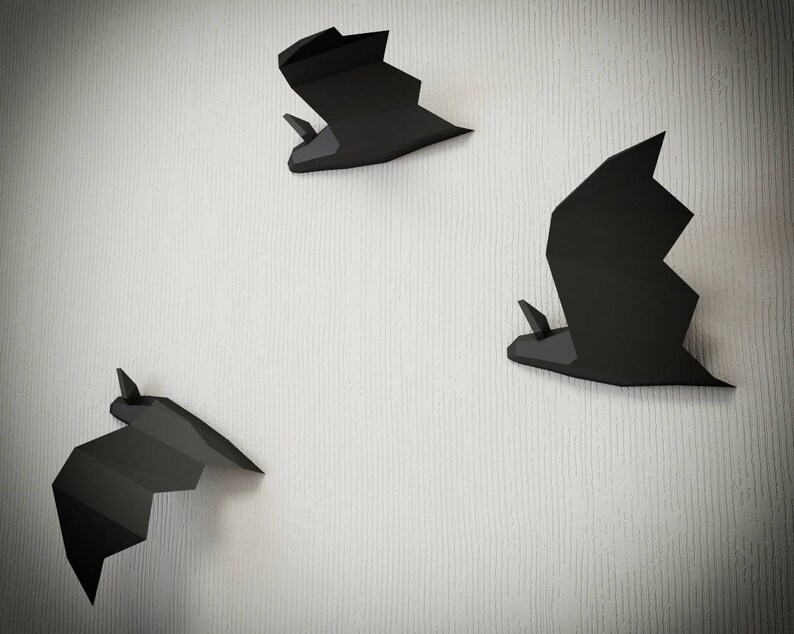 May include: Three black paper bats are mounted on a white textured wall. The bats are in different sizes and positions.
