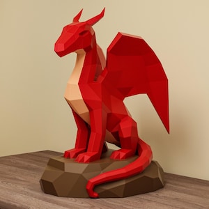 May include: A red geometric dragon sculpture with large wings, sitting on a brown, polygonal base. The dragon has a light tan chest and is posed with its tail curled. The sculpture is displayed on a wooden surface.