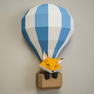 May include: A papercraft hot air balloon with blue and white stripes, with a fox inside the basket. The fox is orange with black eyes and a black nose.