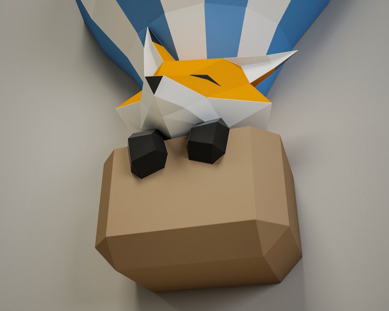 May include: A papercraft fox in a hot air balloon. The fox is orange and white with black eyes and nose. The balloon is blue and white with a brown paper basket.