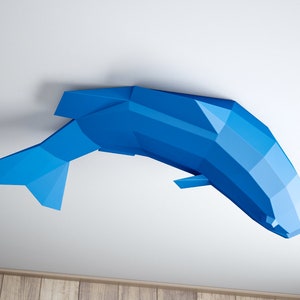 May include: A blue origami fish sculpture hanging from a white ceiling. The fish is made of paper and has a geometric design.