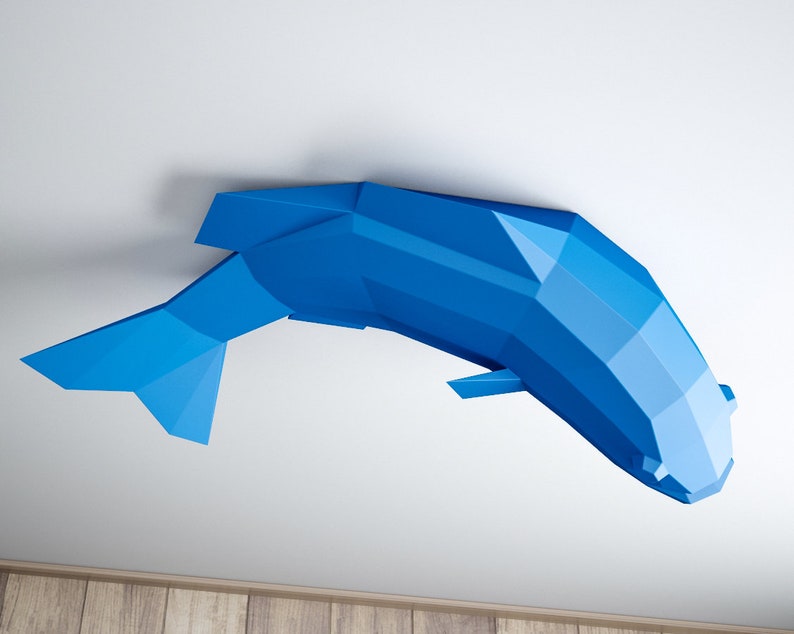 May include: A blue origami fish sculpture hanging from a white ceiling. The fish is made of paper and has a geometric design.