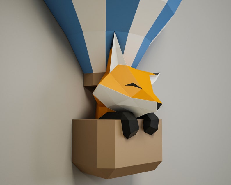 May include: A papercraft fox with orange fur and black eyes is sleeping inside a brown paper hot air balloon with blue and white stripes.