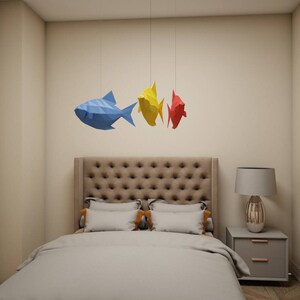 May include: A bedroom with a bed with a tufted headboard and a bedside table with a lamp. Three paper fish mobiles hang from the ceiling, one blue, one yellow, and one red.