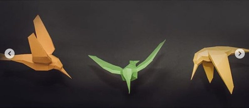 May include: Three origami paper birds in different colors: orange, green, and yellow. The birds are all facing forward and have their wings spread out.