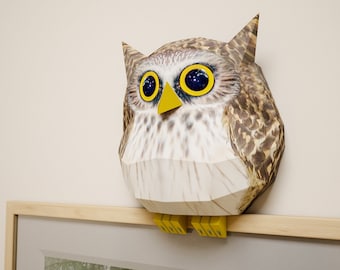 May include: A papercraft owl with brown and white feathers, yellow eyes, and a yellow beak. The owl is perched on a wooden shelf.