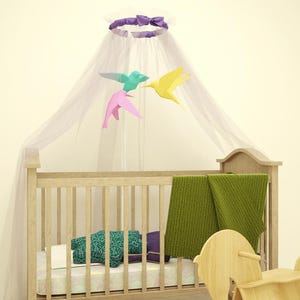 May include: A wooden crib with a white canopy and a mobile with colorful origami birds. The crib has a green blanket and a wooden rocking horse beside it.