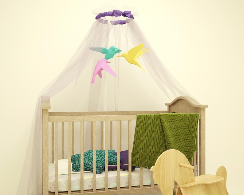 May include: A wooden crib with a white canopy and a mobile with colorful origami birds. The crib has a green blanket and a wooden rocking horse beside it.