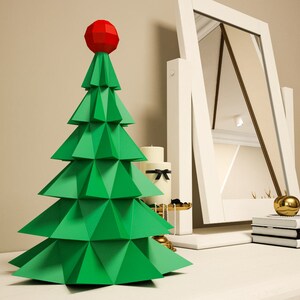 May include: A green paper Christmas tree with a red star on top. The tree is sitting on a white table with a mirror and other decorations.