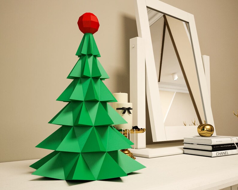 May include: A green paper Christmas tree with a red star on top. The tree is sitting on a white table with a mirror and other decorations.