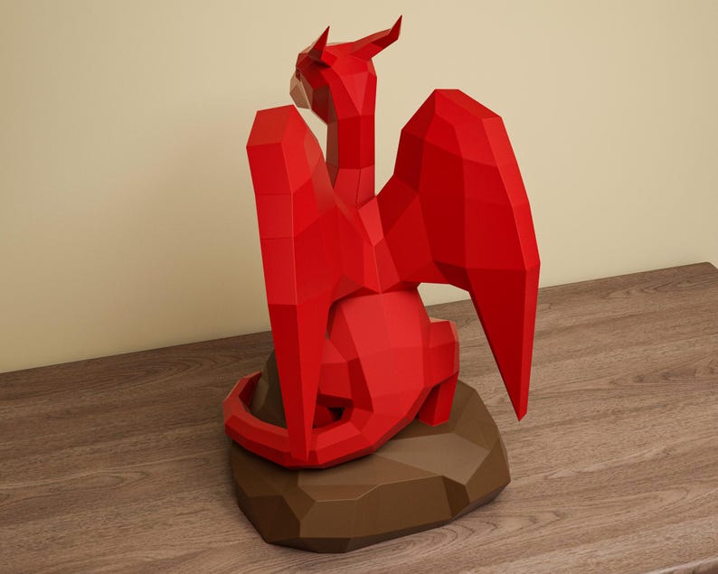 May include: A red, geometric paper dragon sculpture with outstretched wings and a detailed form. The dragon is perched on a brown, polygonal base, creating a striking contrast against the wooden surface.