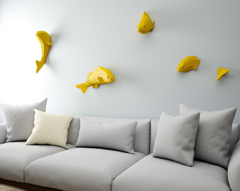 May include: A gray couch with three pillows and a white wall with five yellow origami fish decorations.