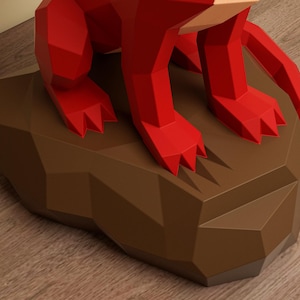May include: A red, geometric sculpture of an animal, possibly a fox, sits on a brown, angular base. The sculpture's form is defined by sharp angles and facets, creating a modern, stylized aesthetic. The base has a faceted design. The sculpture is on a wooden surface.