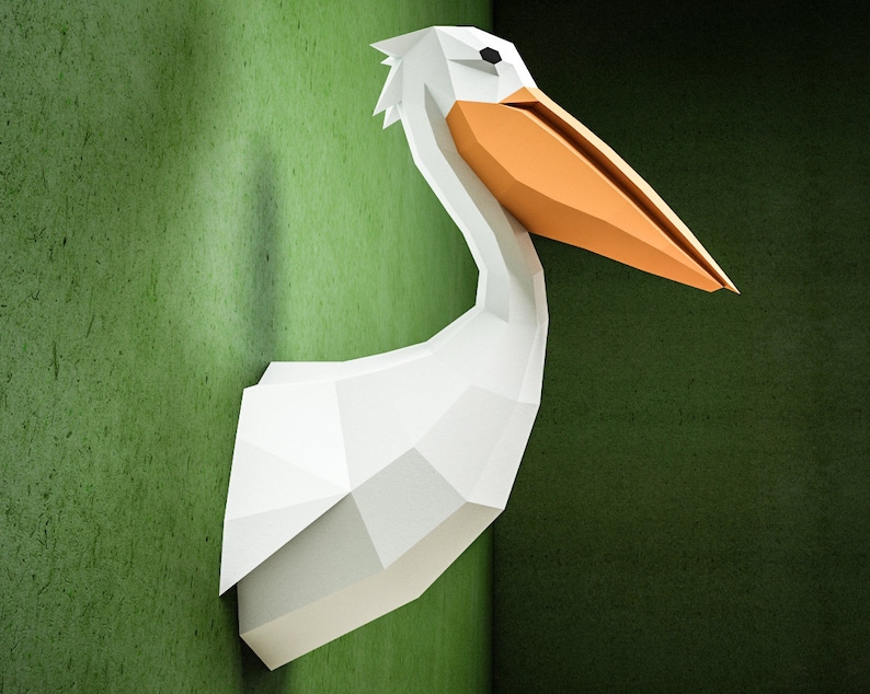 May include: A white origami pelican with an orange beak, mounted on a green wall.
