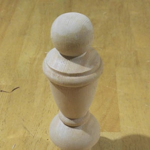 May include: A wooden finial with a rounded top and a fluted design. The finial is unfinished and has a natural wood color.