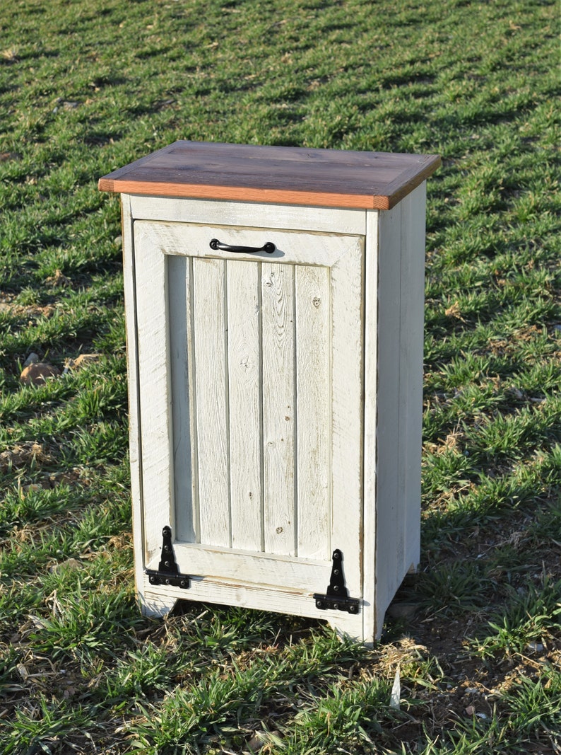 May include: White wooden trash can with a hinged door and black metal hinges. The top is made of a darker wood.