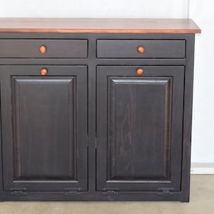 May include: A black wooden cabinet with two drawers and two doors. The cabinet has a brown top and brass knobs.