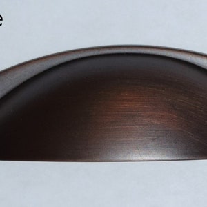 May include: A 5 inch wide,  bronze cabinet pull with a rounded, arched shape.  The pull has a brushed finish.