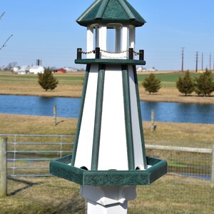 May include: A white and green birdhouse shaped like a lighthouse with a small, white, rounded roof. The birdhouse has a green base and a white post.