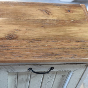 May include: A wooden storage cabinet with a whitewashed finish and a natural wood top. The cabinet has a single door with a black metal handle.