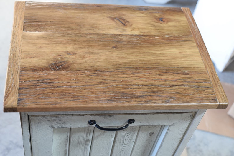May include: A wooden storage cabinet with a whitewashed finish and a natural wood top. The cabinet has a single door with a black metal handle.