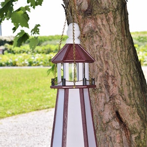 May include: A white and burgundy bird feeder shaped like a lighthouse with a gold chain hanging from a tree. The feeder has a clear plastic window and a hexagonal base.