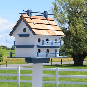 以下が含まれることがあります： 茶色の屋根瓦が付いた白と青の鳥小屋。鳥小屋は複数の区画に分かれており、白い柱に取り付けられています。