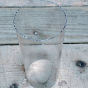 May include: A clear glass cylinder tube, standing upright on a wooden surface.