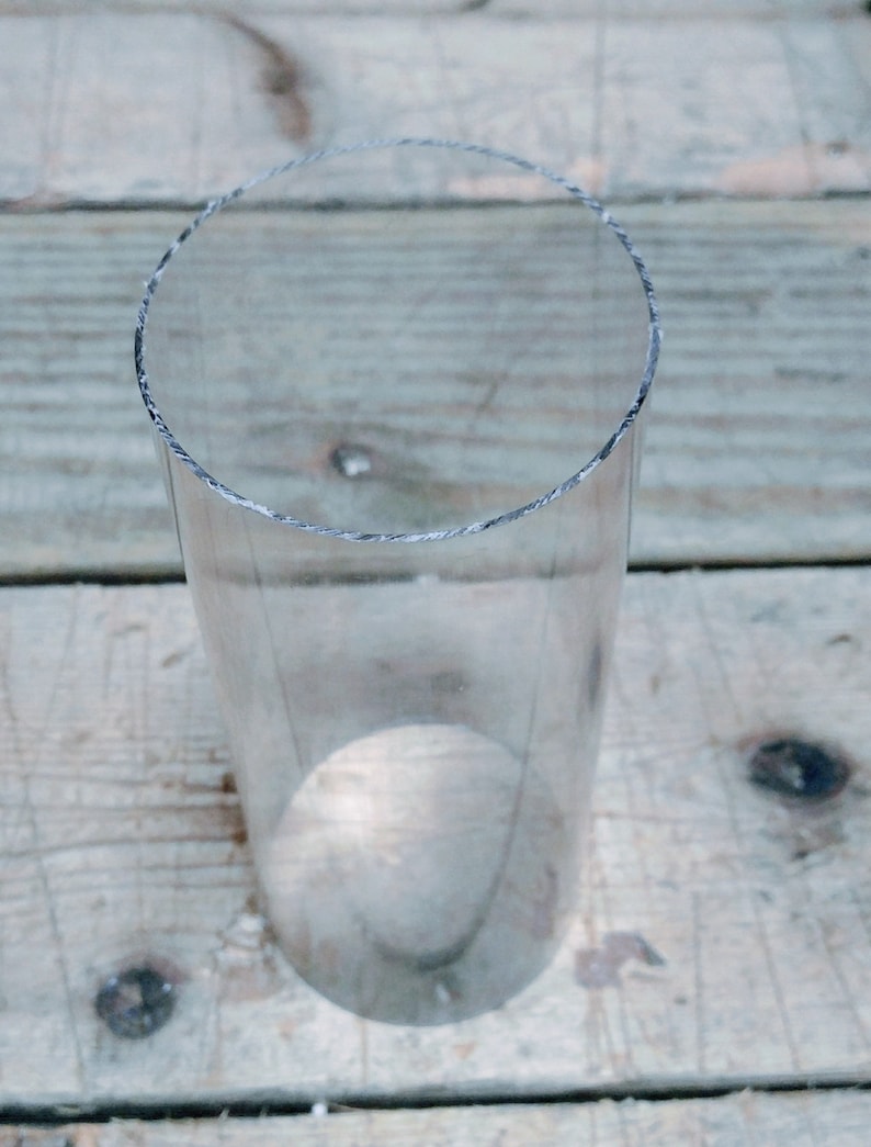 May include: A clear glass cylinder tube, standing upright on a wooden surface.