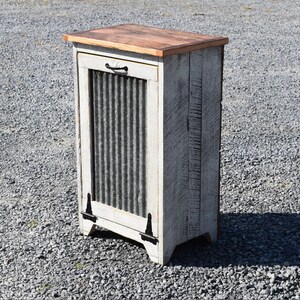 May include: White painted wooden cabinet with a corrugated metal door and a wood top. The cabinet has black hinges and a black handle.
