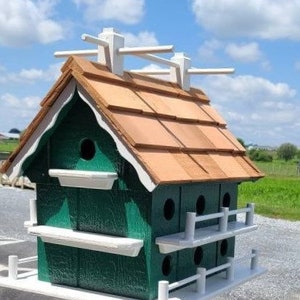 以下が含まれることがあります： 緑と白の鳥小屋。屋根は板葺きで、複数の巣箱があります。鳥小屋には白い手すりがあり、白い土台があります。