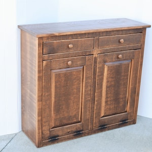 May include: A dark brown wooden cabinet with two drawers and two doors. The cabinet has a rustic finish and black metal hardware.