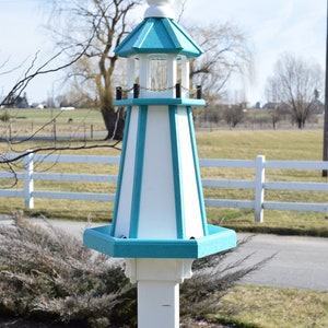 May include: A white and teal blue lighthouse birdhouse with a gold chain hanging from the top. The birdhouse is mounted on a white wooden pole.