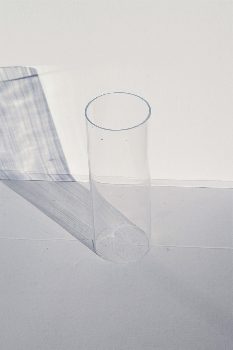 May include: A clear glass cylinder vase, standing on a white surface.