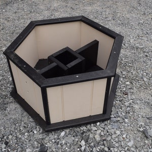 May include: A hexagonal planter made of black and white plastic with a black rim. The planter has a unique design with a central compartment and four smaller compartments around it.