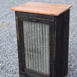 May include: A black wooden cabinet with a corrugated metal door and a wood top. The cabinet has black metal hinges and a black metal handle.