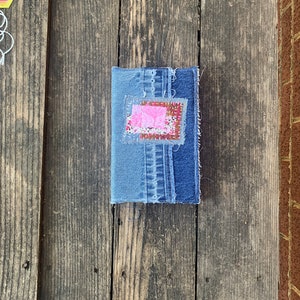 Puede incluir: Un pequeño cuaderno de mezclilla con un parche de tela rosa y rojo cosido en la portada.