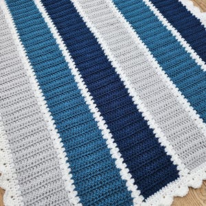 May include: A crocheted baby blanket with a white border and stripes of gray, blue, and teal.
