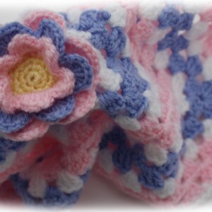 May include: A crocheted baby blanket in pink, white and blue with a large flower in the corner.
