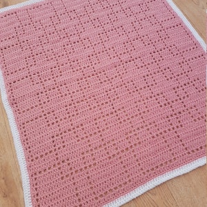 May include: A pink crocheted baby blanket with a white border. The blanket has a delicate, openwork pattern.