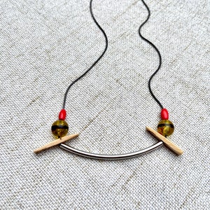 May include: A silver necklace with a curved bar and two wooden pieces on either side. The wooden pieces are attached to red and green beads.