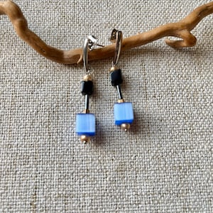 Peut inclure: Une paire de boucles d'oreilles pendantes avec des perles carrées bleues et noires et des créoles argentées.