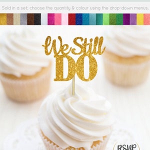 May include: Gold glitter cupcake topper with the text "We Still Do" on a white cupcake.